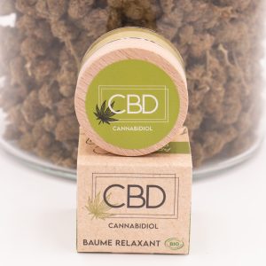Packaging Baume Relaxant CBD Bio MONPLANCBD devant un grand bocal de fleurs de CBD (décor).