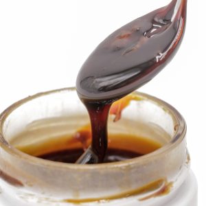 Gros plan sur le Rosin CBD liquide MONPLANCBD (61.83%) coulant d'un outil de dab dans un pot - Meilleur haschisch CBD.